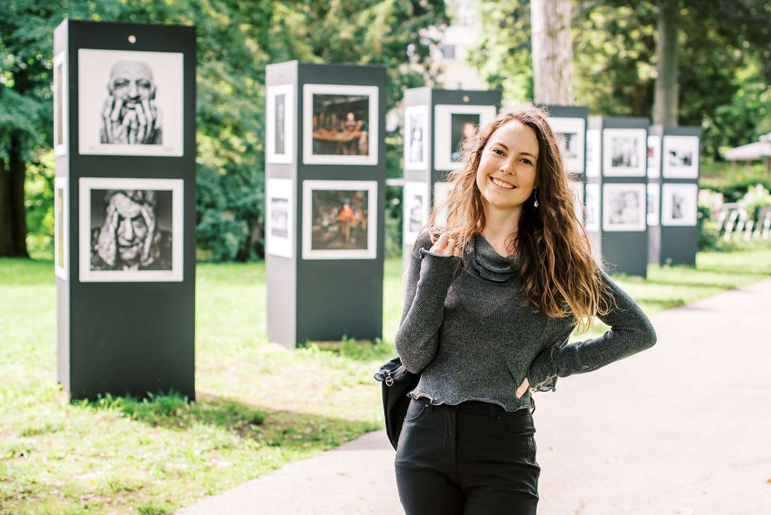 Paris-based photographer Paige Gribb smiling at the Été des Portraits exhibit, with many photos on display behind her
