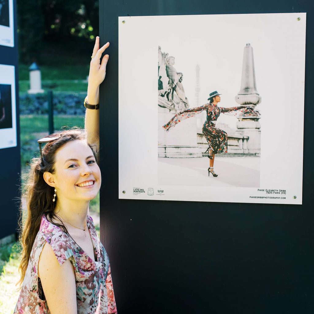 professional photographer Paige Gribb posing next to her work at the Été des Portraits outdoor exhibition in 2021 - closeup square image