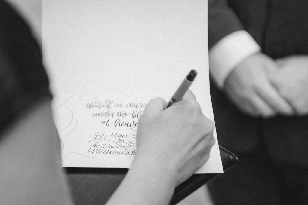 Black and white image of wedding officiant signing a symbolic certificate