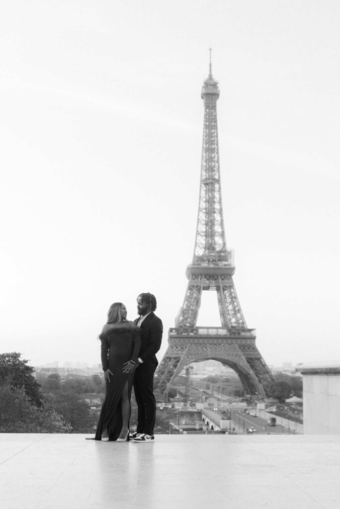 Black and white image of a couple at Place du Trocadero, gazing at each other with the full Eiffel Tower in the background at the beginning of their engagement session.