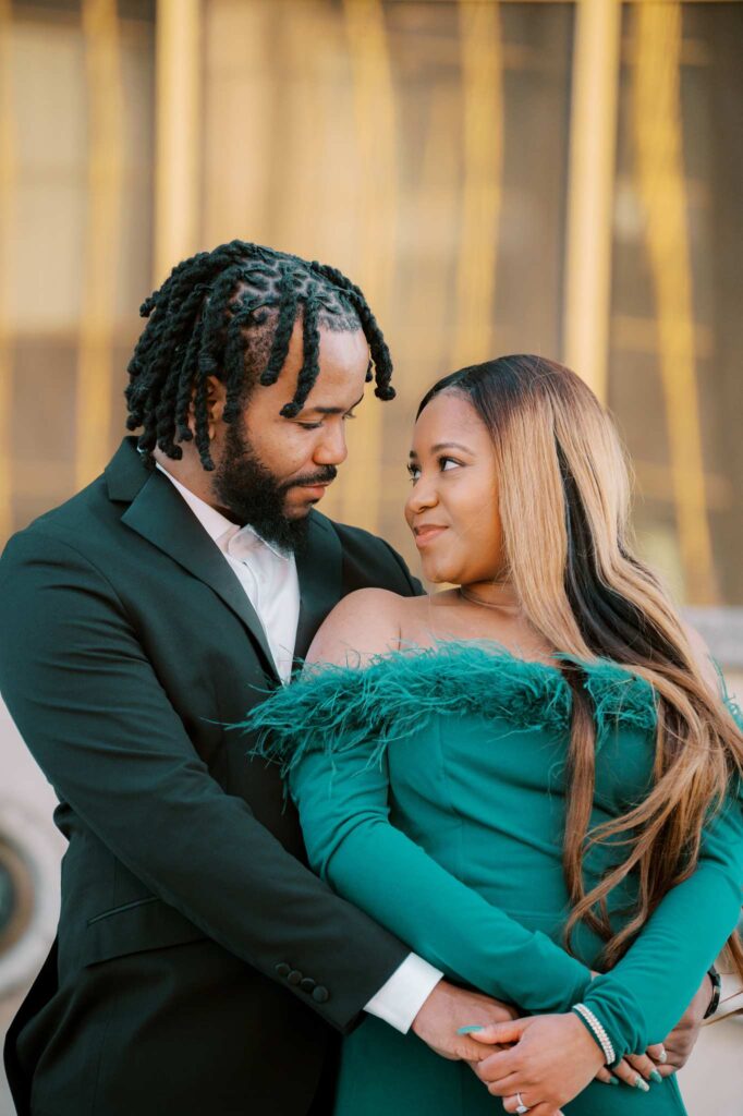 A man in twists and a suit embraces his partner from behind during their engagement photoshoot in Paris. Both are dressed up and they look at each other lovingly while holding hands.