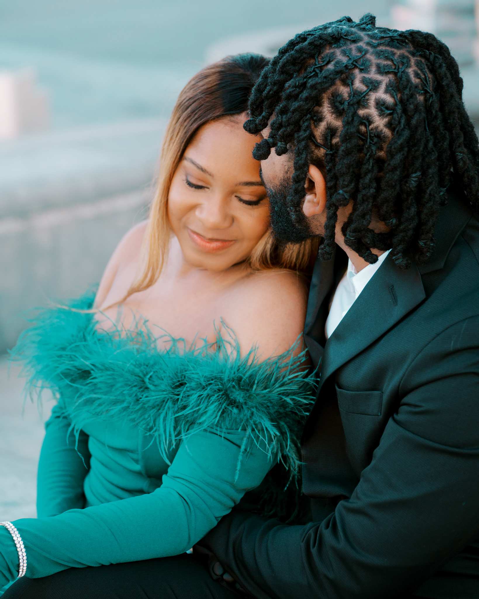 A Black man in a suit with twists in his hair holds his fiancée from behind and kisses her forehead, while she closes her eyes and smiles contentedly. Example of couples photography by Amsterdam based photographer Paige Gribb