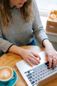 A person works on culling photos on a laptop at a cafe with a cappuccino next to her.
