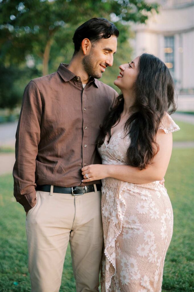 A couple stands in the park on a sunny morning, smiling and looking into each other's eyes during their anniversary celebration.