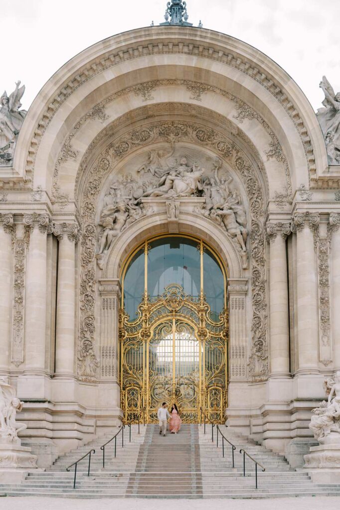 The grand, ornate entrance to the Petit Palais with its large golden doorway in an intricately carved archway makes the perfect backdrop for a memorable photo shoot in Paris. Two people celebrating their 5th Anniversary, walk down the steps together while holding hands.