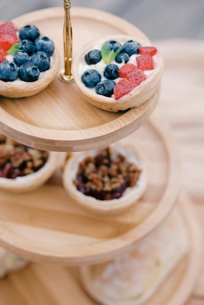 Mini fruit tarts with blueberries and strawberries on a wooden tiered dessert stand, perfect for a surprise proposal or elegant proposal photo shoot.