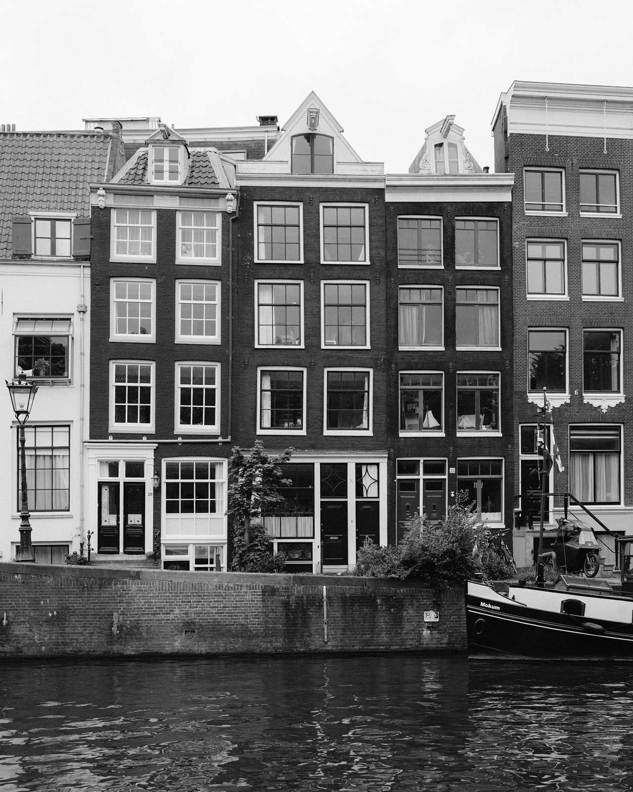 Black and white photo of tall, narrow Amsterdam canal houses with many windows, next to water and a boat—an ideal spot for memorable proposal photography.