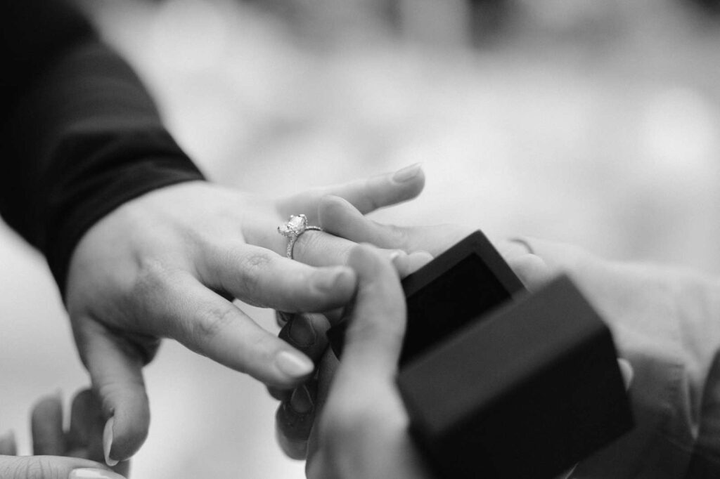 Close-up of a person placing an engagement ring on another's finger, with an open ring box nearby—perfect for a romantic proposal photo shoot.