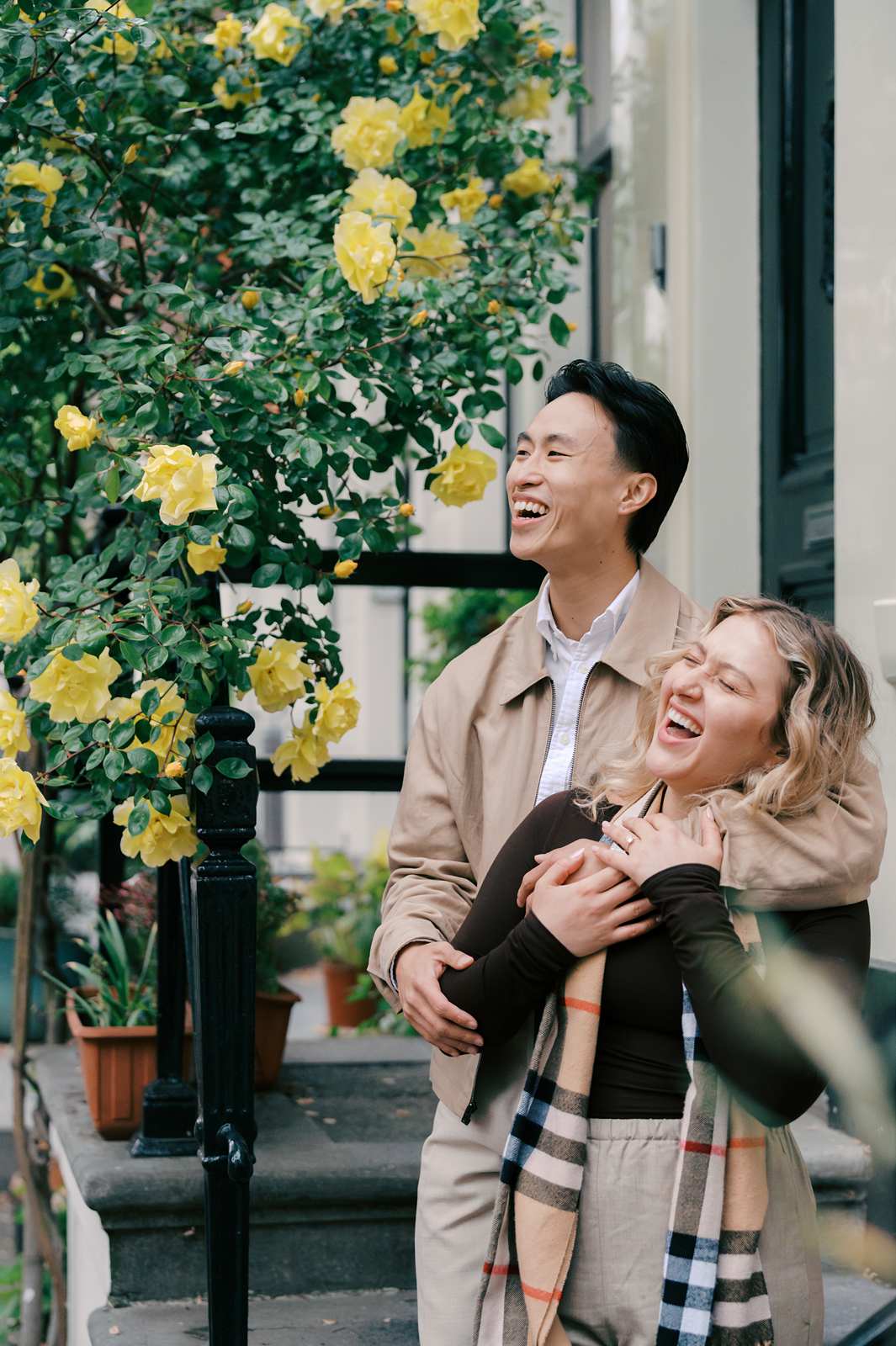 A smiling couple stands together by yellow roses in Amsterdam, enjoying a happy moment outside—perfect for proposal photography.