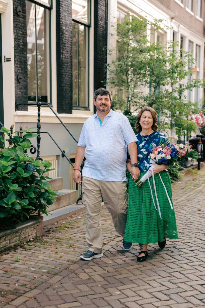 A couple walks hand in hand on a cobblestone street in Amsterdam; the woman holds a custom bouquet of colorful flowers, perfect to celebrate their anniversary in Amsterdam.