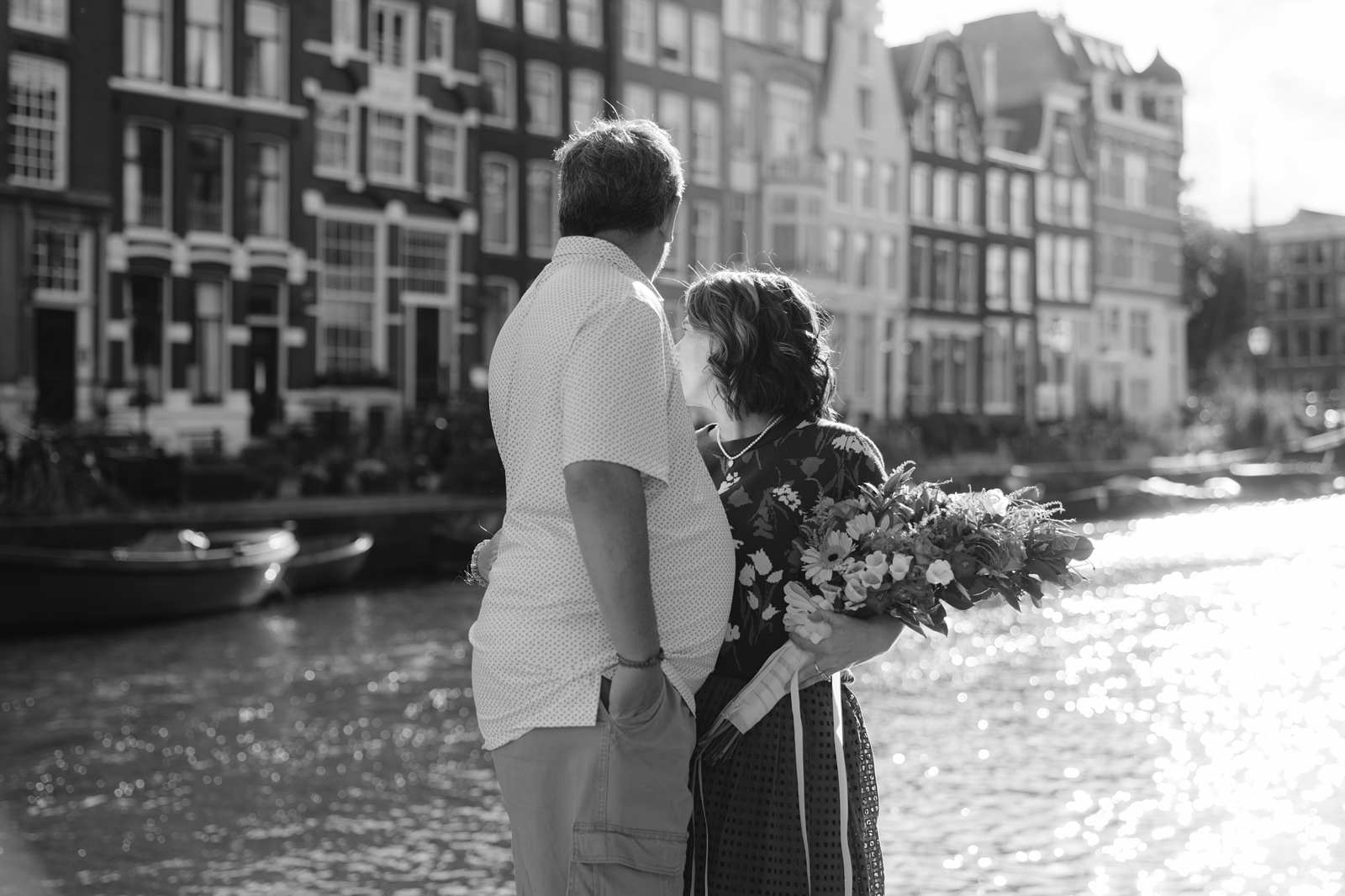 Black and white photo of a couple looking out at an Amsterdam canal at golden hour