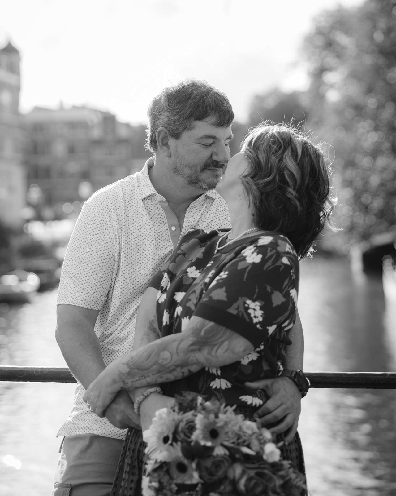 Black and white image of an about-to-kiss moment as the couple holds each other while standing on a bridge