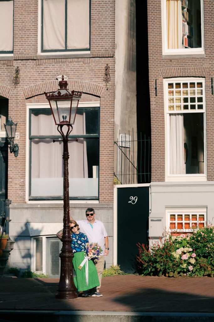 A couple leans on a lamppost in direct sunlight, wearing sunglasses, for a memorable and badass moment during their Amsterdam photo shoot.