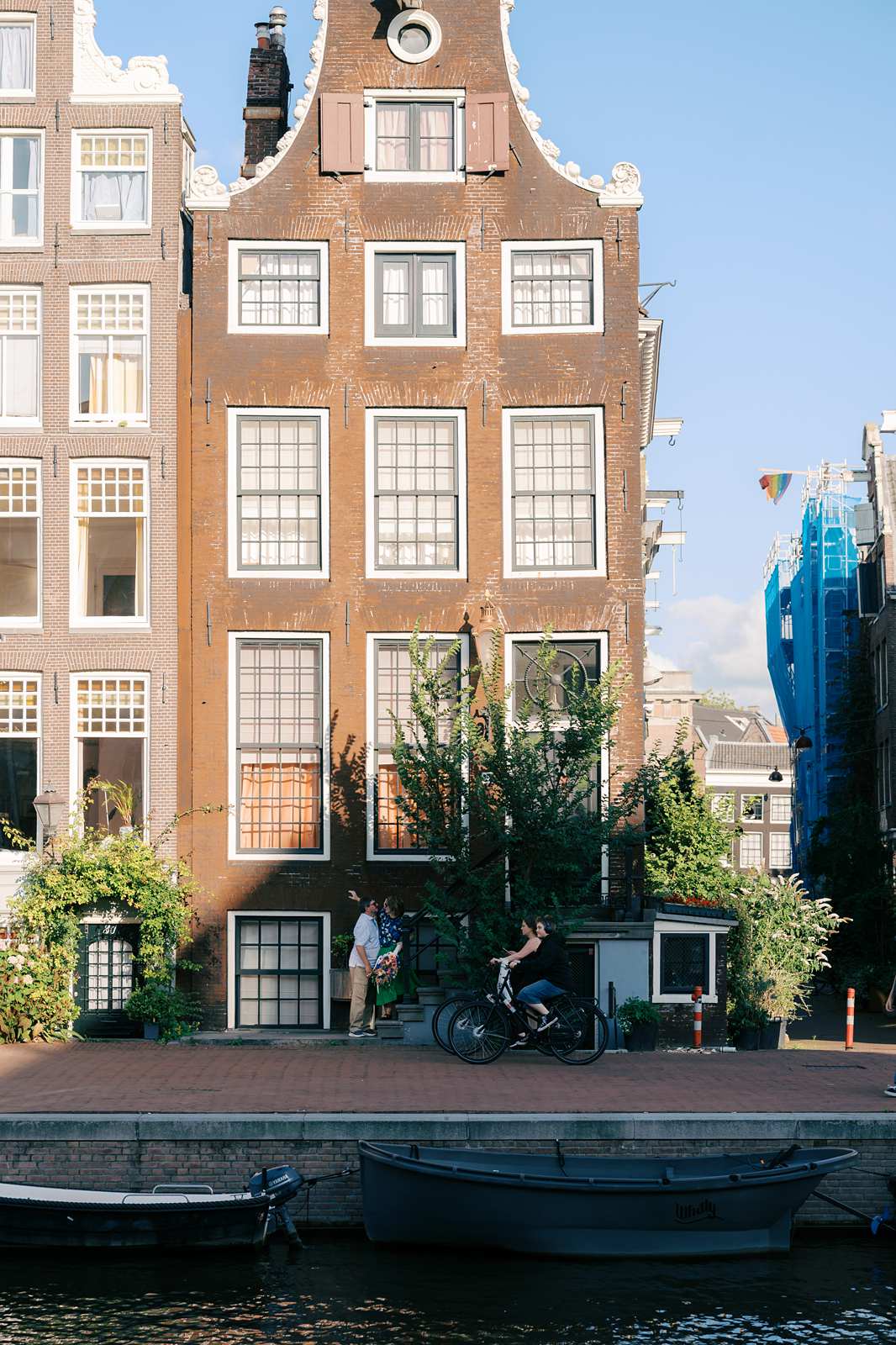A couple kisses in front of a brick building in Amsterdam as someone bikes past them during their photo shoot