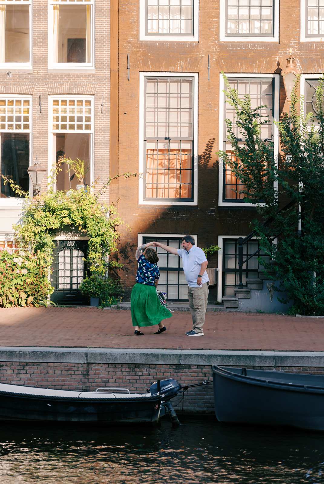A woman spins under her husband's arm as they dance together on a canal-side walkway in Amsterdam
