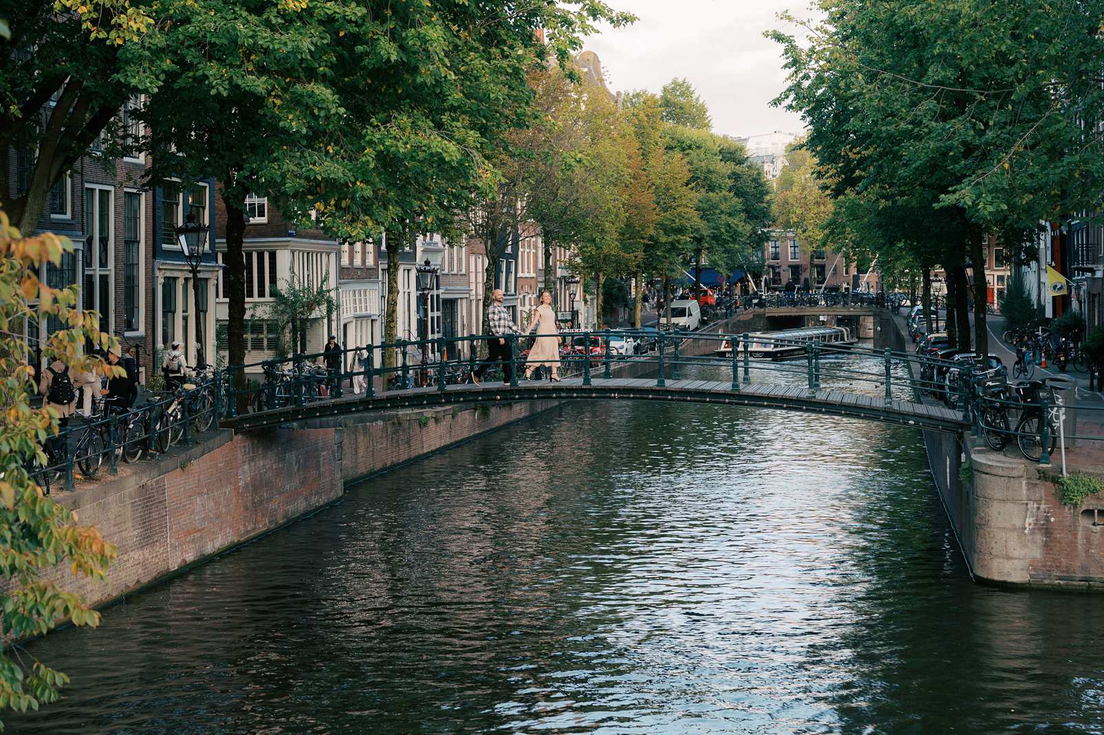 A scenic canal in Amsterdam with a walking bridge, trees, and buildings along the water—perfect for capturing engagement photos if you’ve recently engaged.