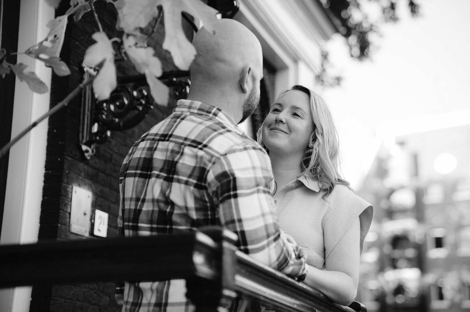 A couple stands on a balcony in Amsterdam, smiling at each other during golden hour in this black-and-white photo.