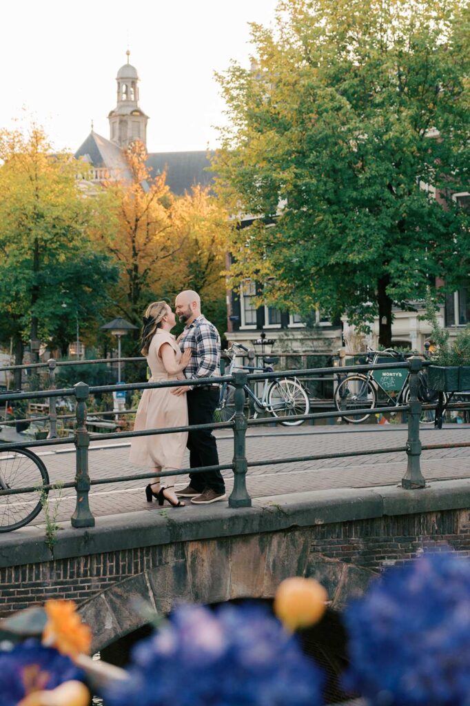 A couple embraces on a bridge in charming Amsterdam, surrounded by trees and bicycles—a perfect romantic fall photo shoot.